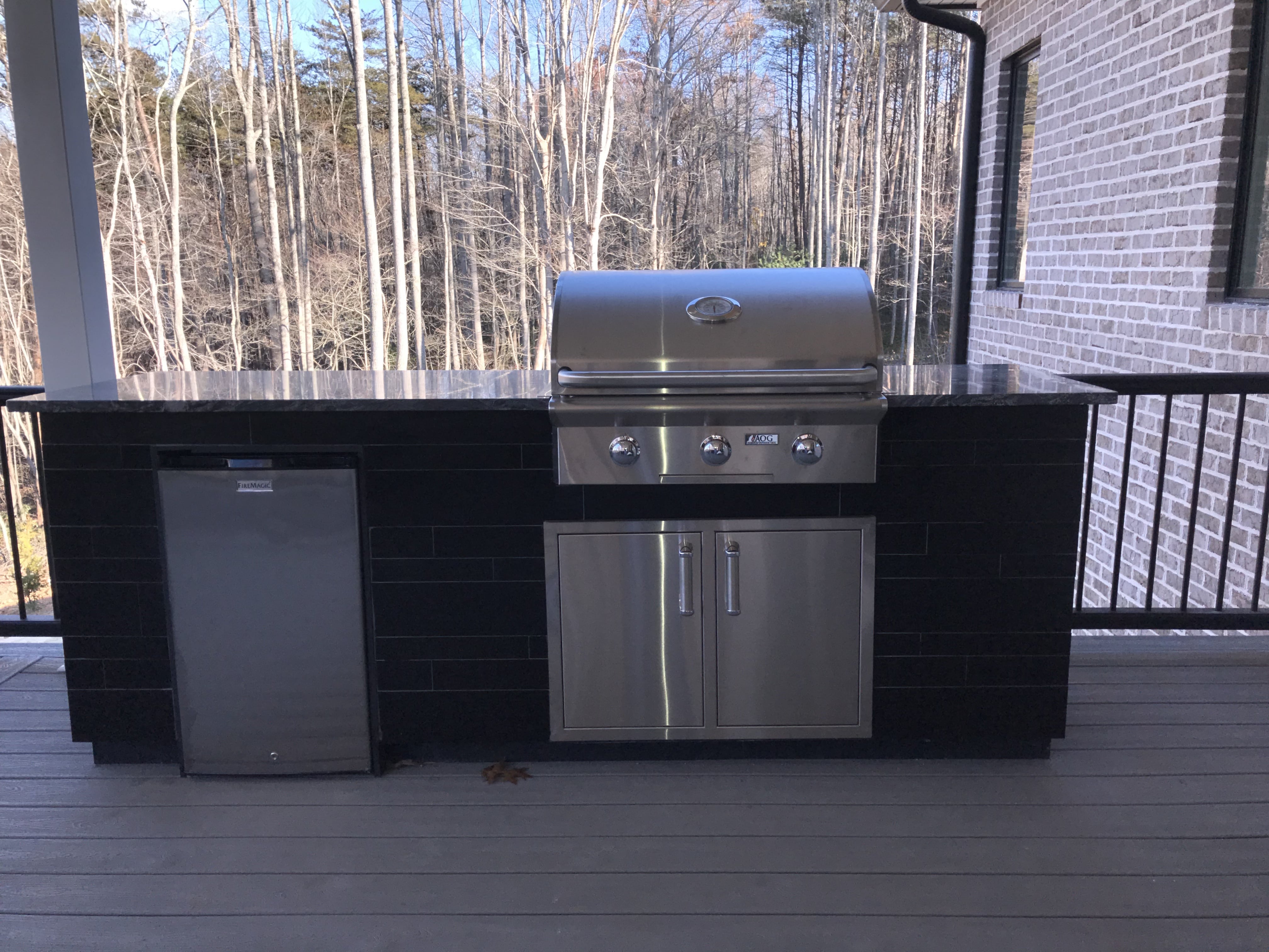 Norstone Ebony Planc Large Format Tile Being installated as the veneer on a residential outdoor kitchen project with stainless steel grill and refrigerator